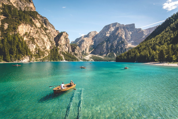 A boat floats serenely on the clear water of a tranquil mountain lake surrounded by lush greenery.